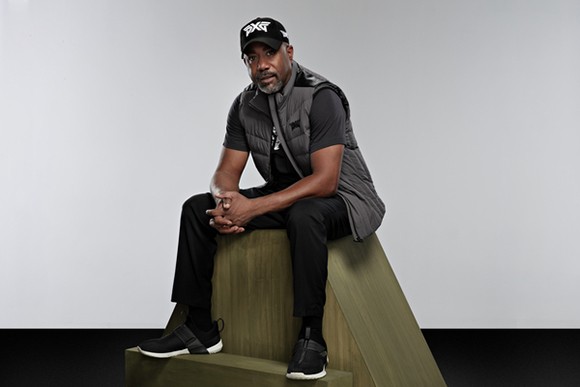 Darius Rucker sitting on a photo set, wearing a PXG hat