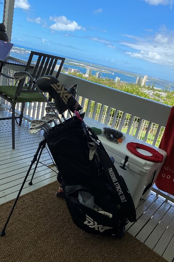 Black PXG golf bag sitting on deck with ocean in background.