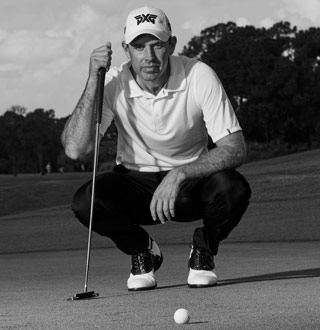 Charl Schwartzel squatting down above a golf ball, holding a PXG club on a golf course
