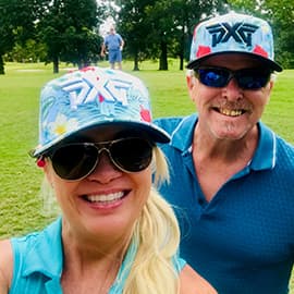 Man and woman smiling in hats on golf course.